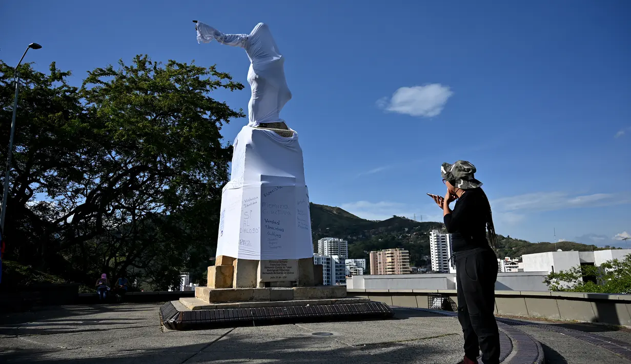 Seorang wanita berbicara di ponselnya saat dia melihat patung penakluk Spanyol abad ke-16 Sebastian de Belalcazar yang ditutupi dengan kain putih sebagai penolakan terhadap ancaman baru-baru ini oleh kelompok adat untuk merobohkannya, di Cali, Kolombia (21/9/2020). (AFP/Luis Robayo)