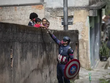 Petugas polisi militer Everaldo Pinto, berkostum superhero Captain America, menyapa anak-anak di tengah pandemi COVID-19 di Petropolis, Rio de Janeiro, Brasil, Kamis (15/4/2021). Pinto memberitahu anak-anak tentang perlunya melindungi diri dari virus corona. (AP Photo/Silvia Izquierdo)
