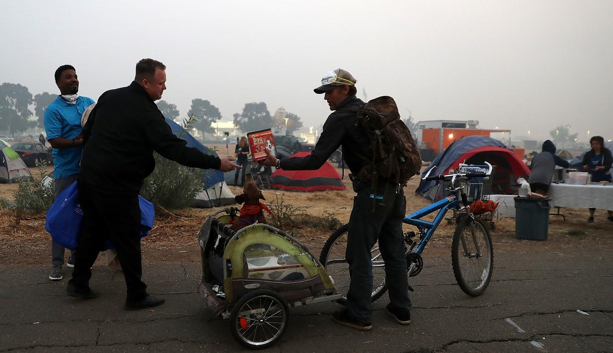 Relawan memberikan makanan anjing kepada pengungsi korban kebakaran di pusat pengungsian di tempat parkir Walmar, Chico, California (16/11). Kebakaran ini merupakan yang terparah dalam sejarah California. (AFP Photo/Justin Sullivan)