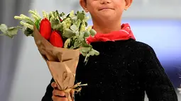 Anak laki-laki dengan down syndrome membawa buket bunga saat ambil bagian di atas catwalk pekan mode Petite Fashion Week di Madrid, 6 Oktober 2017. Tampil dalam balutan busana, mereka tampak menikmati tugasnya sebagai model. (GABRIEL BOUYS/AFP)