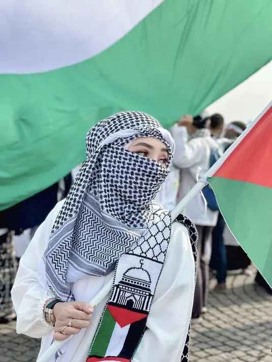 Ia tampak mengenakan kafayeh dan gamis putih. Tak ketinggana syal dengan aksen bendera Palestina menjadi pernyataan gayanya. [Instagram/ ShellaSaukia]