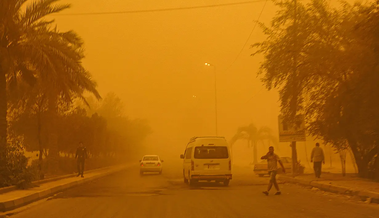 Pejalan kaki menyeberang jalan saat kendaraan melaju di tengah badai debu berat di Baghdad, Irak, Senin (16/5/2022). (Sabah ARAR/AFP)