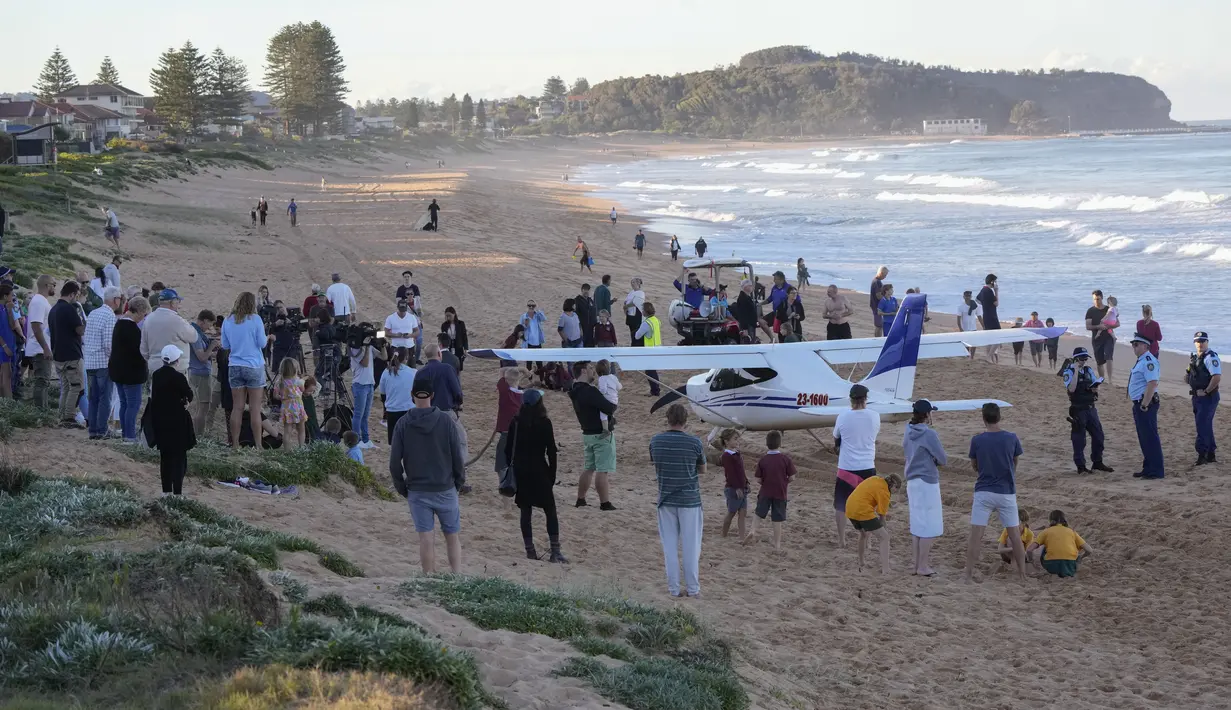 Orang-orang berdiri di dekat sebuah pesawat ringan yang mendarat darurat di sebuah pantai di Sydney, Rabu (26/5/2021). Pesawat kategori rekreasi itu mendarat selamat di pantai Sydney dengan tiga orang di dalamnya termasuk seorang bayi setelah mengalami kerusakan mesin. (AP Photo/Mark Baker)