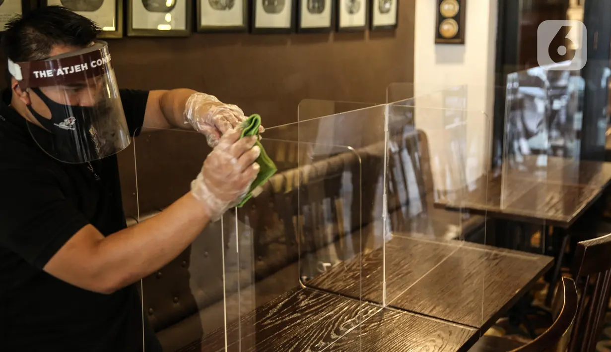 Pekerja membersihkan papan pelindung akrilik usai digunakan pengunjung di The Atjeh Connection Coffee and Resto, Jakarta, Senin (8/6/2020). Tempat ini siap menerapkan protokol kesehatan dalam menerapkan tatanan kehidupan baru atau ‘new normal’. (Liputan6.com/Faizal Fanani)