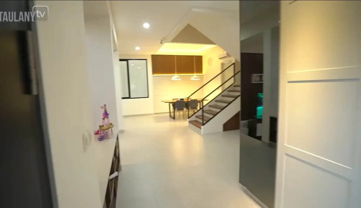 Ruangan tampak sangat luas dengan dominasi warna dinding putih dan semakin terlihat indah dengan saat kena sinar lampu. Akses tangga ke atas untuk kamar utama dan anak-anaknya. [Youtube/TAULANY TV]