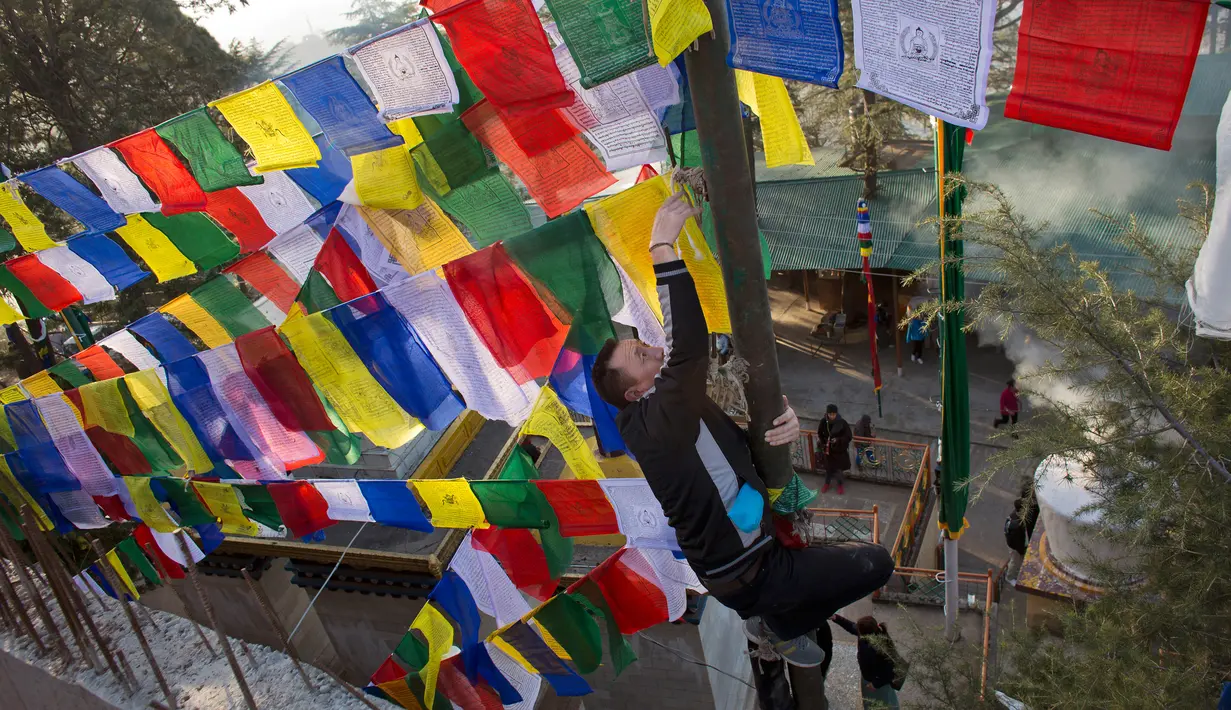 Seorang pria memasang bendera warna-warni atau yang disebut lungta pada hari ketiga Tahun Baru Tibet di Dharmsala, India (18/2). Bendera doa itu merupakan barang yang sakral sekaligus suvenir unik yang seringkali dibawa turis. (AP/Ashwini Bhatia)