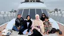 Potret bahagia Happy Salma bersama keluarganya di atas kapal. Happy Salma yang berpose di tengah tampil anggun dengan abay hitam, ditumpuk lagi dengan atasan cokelat muda yang serasi dengan hijabnya. [Foto: Instagram/happy_asmara77]