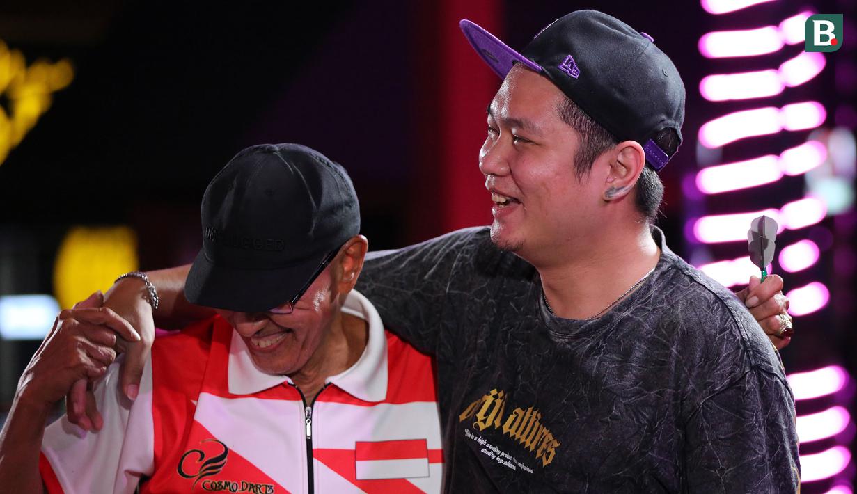 Pemain Darts, Tirta Suparjo (kanan) dan Haji Suwendi bercengkrama saat berkompetisi dalam turnamen Darts National Competition series 2 yang berlangsung di Sedayu City, Jakarta, Minggu (28/04/2024). Tirta berhasil mempertahankan gelar juara setelah menang atas Haji Suwendi dengan skor 3-1. (Bola.com/Revi Muzaki)