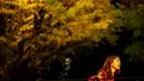 Seorang perempuan berpose dengan latar pohon ginkgo dalam warna musim gugur di Taman Luar Kuil Meiji di Tokyo, Kamis (18/11/2021). Pada pertengahan bulan November, barisan pohon ginkgo yang ada di taman ini akan berubah warna menjadi kuning keemasan. (Philip FONG / AFP)