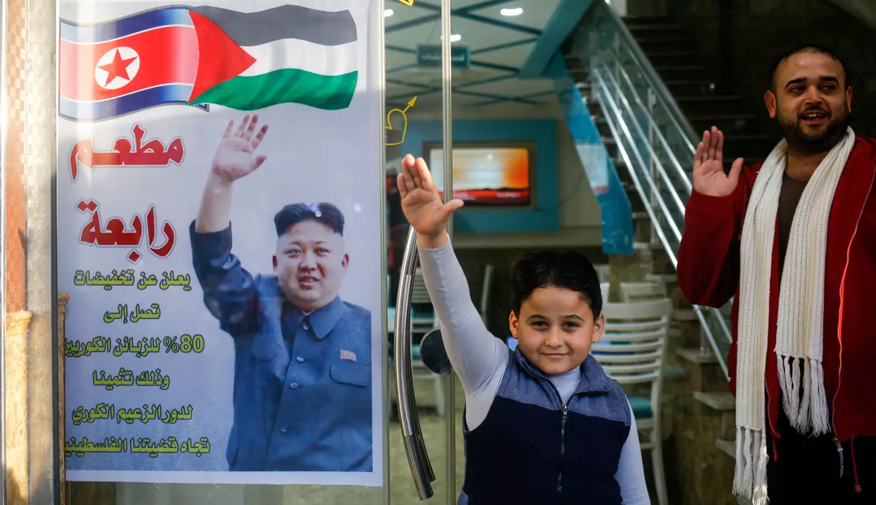 Salam Rabaa dan anaknya meniru pose pemimpin Korea Utara, Kim Jong-un pada poster di pintu restoran Rabaa di kamp pengungsi Jabalia, Gaza, Minggu (17/12). Restoran itu menawarkan potongan harga besar untuk pengunjung asal Korea Utara. (MOHAMMED ABED/AFP)