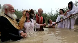 Imam Kristen Ortodoks Serbia membaptis wanita di perairan Sungai Yordan di dekat kota Jericho (4/3). Sungai ini diyakini menjadi tempat Yesus Kristus dibaptis oleh Yohanes Pembaptis.  (AFP Photo/Gali Tibbon)