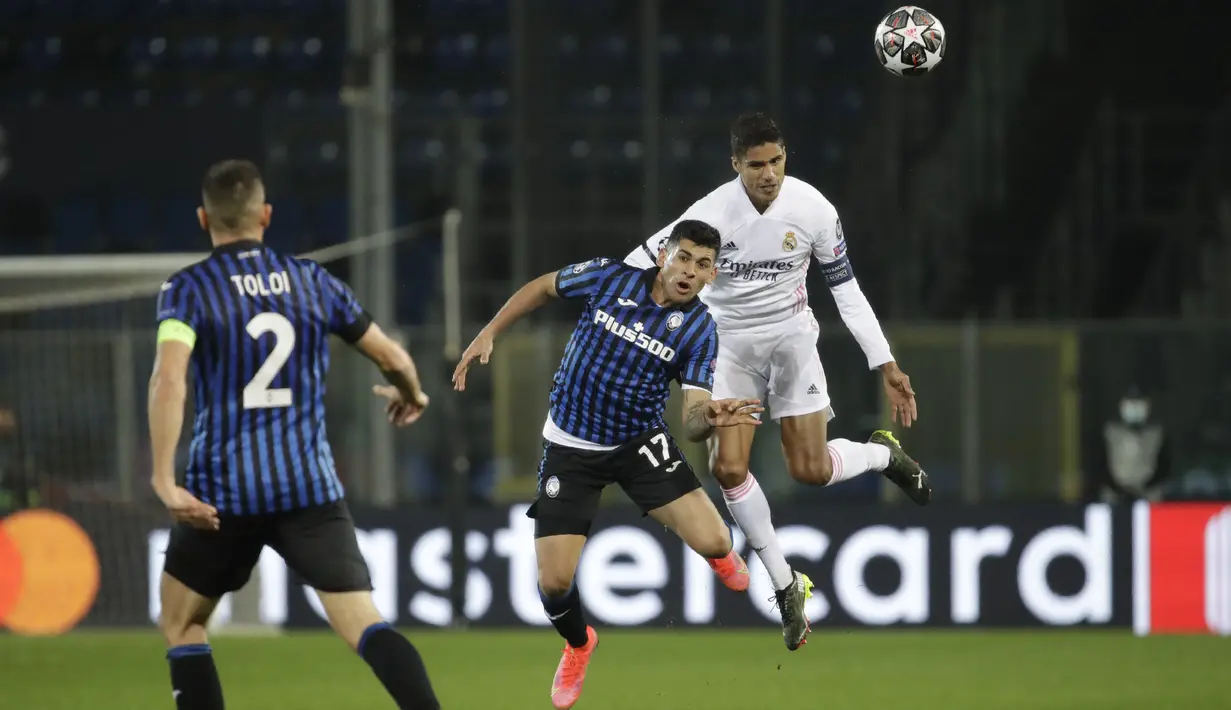 Bek Real Madrid, Raphael Varane melompat untuk merebut bola dari bek Atalanta, Cristian Romero pada leg pertama babak 16 besar Liga Champions di Stadion Gewiss, Kamis (25/2/2021) dini hari WIB. Real Madrid harus susah payah kalahkan Atalanta 1-0. (AP Photo/Luca Bruno)