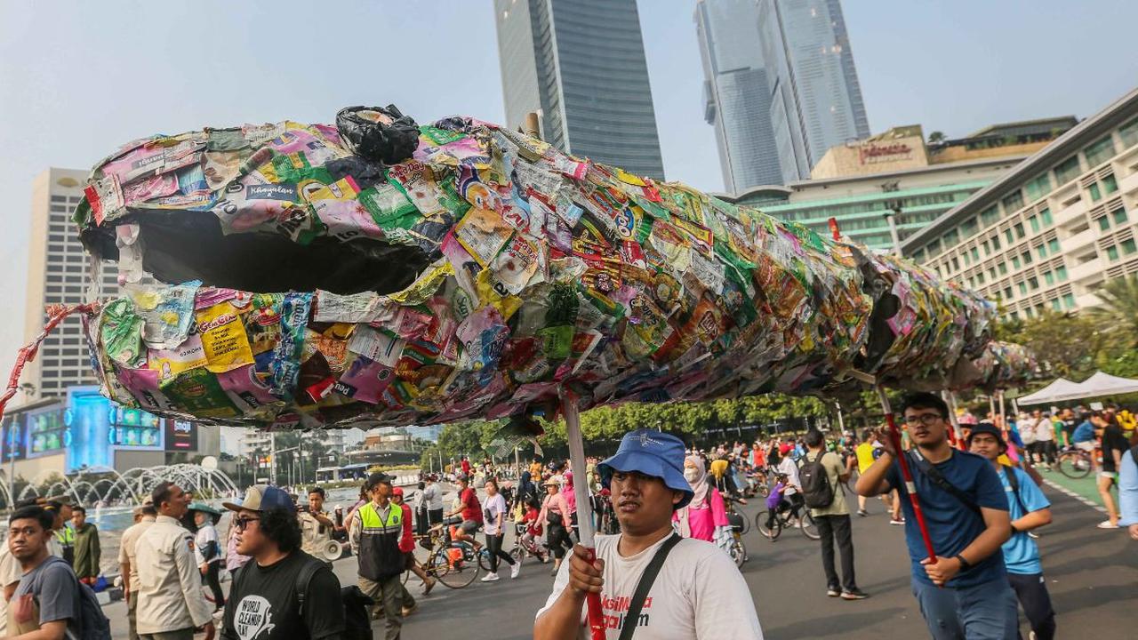 Pegiat lingkungan membawa poster hingga instalasi ular dari sampah plastik saset saat menggelar pawai bebas plastik di Kawasan Sudirman, Jakarta, Minggu (30/7/2023).