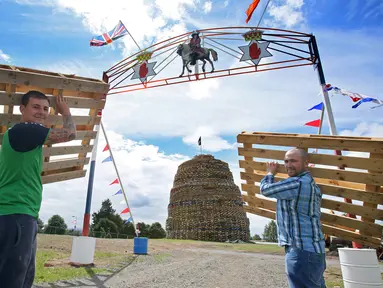 Dua orang pria membawa palet kayu yang akan disusun untuk membuat api unggun di Ballymacash, Lisburn, Irlandia (10/7). Api unggun raksasa ini dinyalakan setiap tahun di Irlandia Utara pada malam 11 Juli. (AFP Photo/Paul Faith)