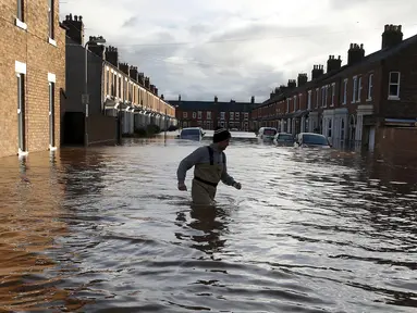 Seorang pria melintasi banjir yang merendam jalan pemukiman di Carlisle, Inggris, Minggu (6/12). Puluhan ribu rumah tidak punya listrik karena Badai Desmond yang menyebabkan banjir di Inggris utara dan sebagian Skotlandia. (REUTERS/Phil Noble)