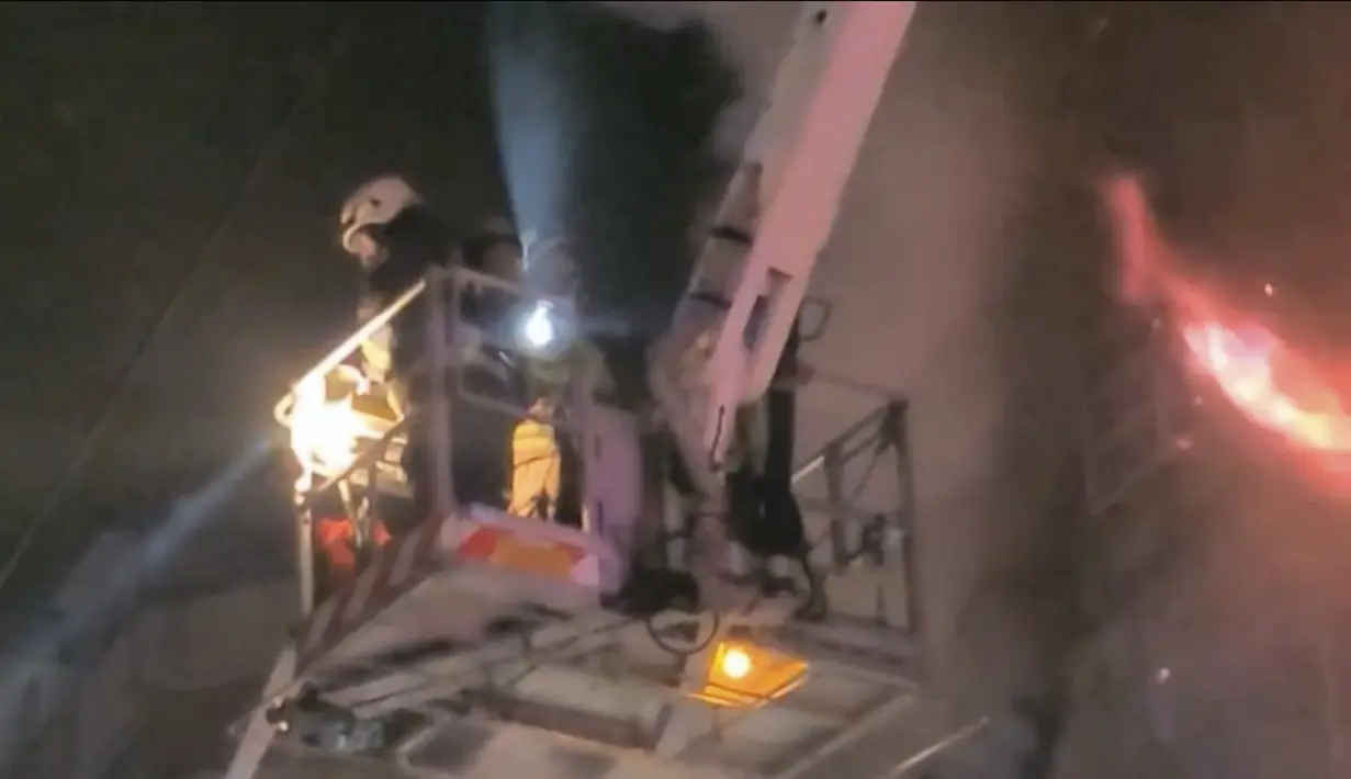 Petugas pemadam kebakaran di atas derek memadamkan api gedung di Kaohsiung, Taiwan selatan, (14/10/2021). Sedikitnya 46 orang tewas dan puluhan lainnya terluka parah dalam kebakaran di blok menara 13 lantai di Taiwan selatan, kata para pejabat. (EBC via AP )