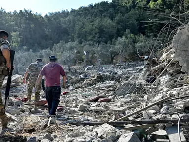 Tentara tentara Lebanon dan lainnya berjalan melewati reruntuhan bangunan yang hancur di lokasi serangan udara Israel sebelumnya di desa Aito, Lebanon utara pada 15 Oktober 2024. (JOSEPH EID/AFP)