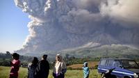 Orang-orang menyaksikan Gunung Sinabung memuntahkan material vulkanik saat meletus di Karo, Sumatera Utara, Selasa (2/3/2021).  Gunung Sinabung, Sumatera Utara, memuntahkan awan panas pada pukul 07.11 WIB, Selasa (2/1/2021). (AP Photo)