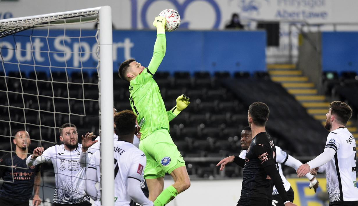 Kiper Swansea City, Freddie Woodman berhasil menjangkau bola dari ancaman pemain Manchester City dalam laga babak kelima Piala FA 2020/21 di Liberty Stadium, Rabu (10/2/2021). Swansea City kalah 1-3 dari Manchester City. (AFP/Rebecca Naden/Pool)