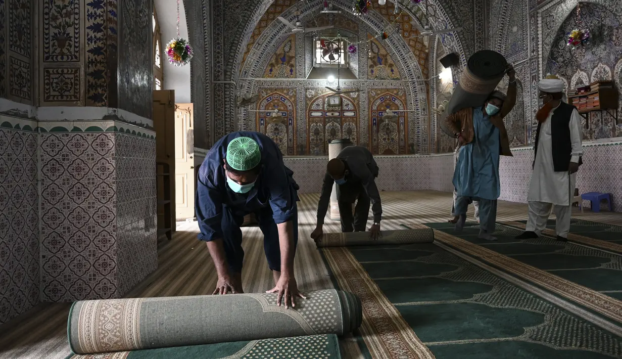 Umat Muslim menggulung karpet sajadah dari aula utama masjid menyusul pembatasan baru pemerintah baru menjelang bulan suci Ramadan di Rawalpindi, Pakistan, Senin (5/4/2021). Lantai masjid juga harus dibersihkan dengan larutan klorin dalam air. (Aamir QURESHI/AFP)