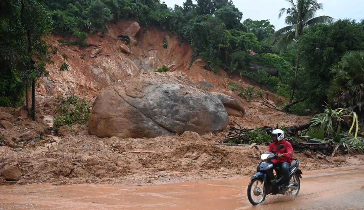 Pengendara motor melihat sebuah batu besar usai tanah longsor di Paung, negara bagian Mon (9/8/2019). Tanah longsor yang disebabkan oleh hujan lebat menewaskan sedikitnya 13 orang dan melukai puluhan lainnya di Myanmar timur. (AFP Photo/Ye Aung Thu)