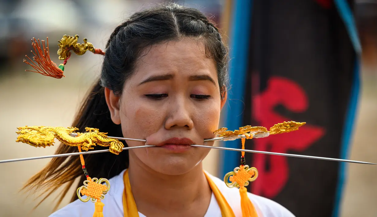 Seorang wanita menusuk pipinya dengan besi  saat mengikuti prosesi perayaan Festival Vegetarian tahunan di Phuket, Thailand, Kamis (3/10/2019). Festival menyiksa diri ini dipercaya bagi warga Phuket akan mendapat kesehatan dan ketenangan pikiran. (AFP Photo/Mladen Antonov)