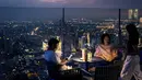 Orang-orang minum dengan latar belakang cakrawala Bangkok di dek observasi gedung pencakar langit King Power Mahanakhon pada 25 Oktober 2021. Gedung tertinggi di Thailand itu juga membuka rooftop bar dan lokasi lantai tembus pandang seluar 63 meter persegi. (Jack TAYLOR / AFP)