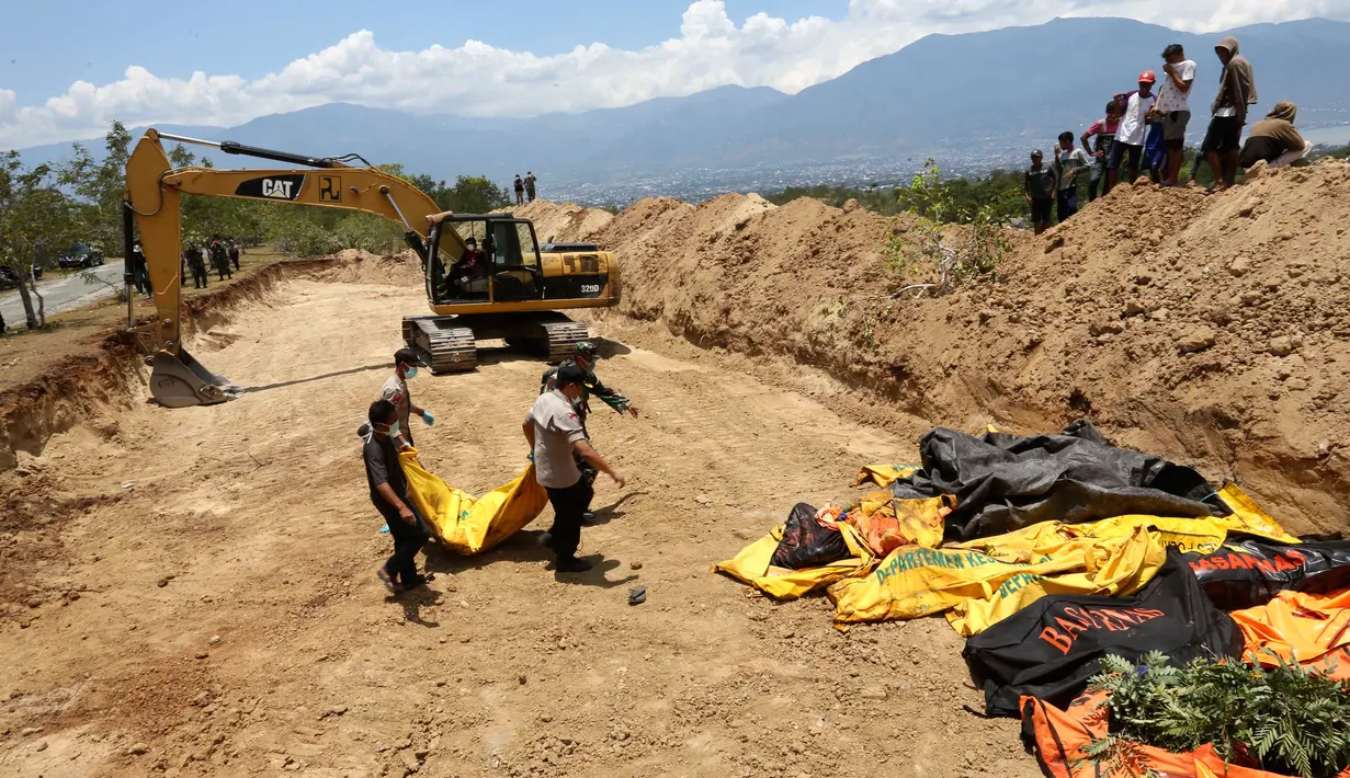 Petugas membawa jenazah korban gempa dan tsunami untuk dimakamkan massal di Palu, Sulawesi Tengah, Senin (1/10). Lokasi pemakaman, telah digali liang besar sejumlah jenazah dimakamkan bersamaan dan dilakukan secara bertahap. (AP Photo/Tatan Syuflana)