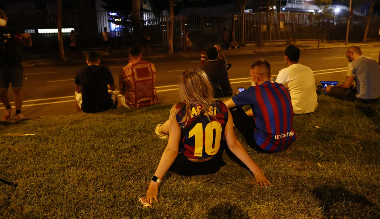 Seorang fans wanita mengenakan kaus replika nomor 10 Lionel Messi duduk di luar stadion Camp Nou di Barcelona (5/8/2021). Para fans berkumpul di depan stadion setelah Barcelona dan Lionel Messi sama-sama sepakat untuk resmi berpisah. (AP Photo/Joan Monfort)