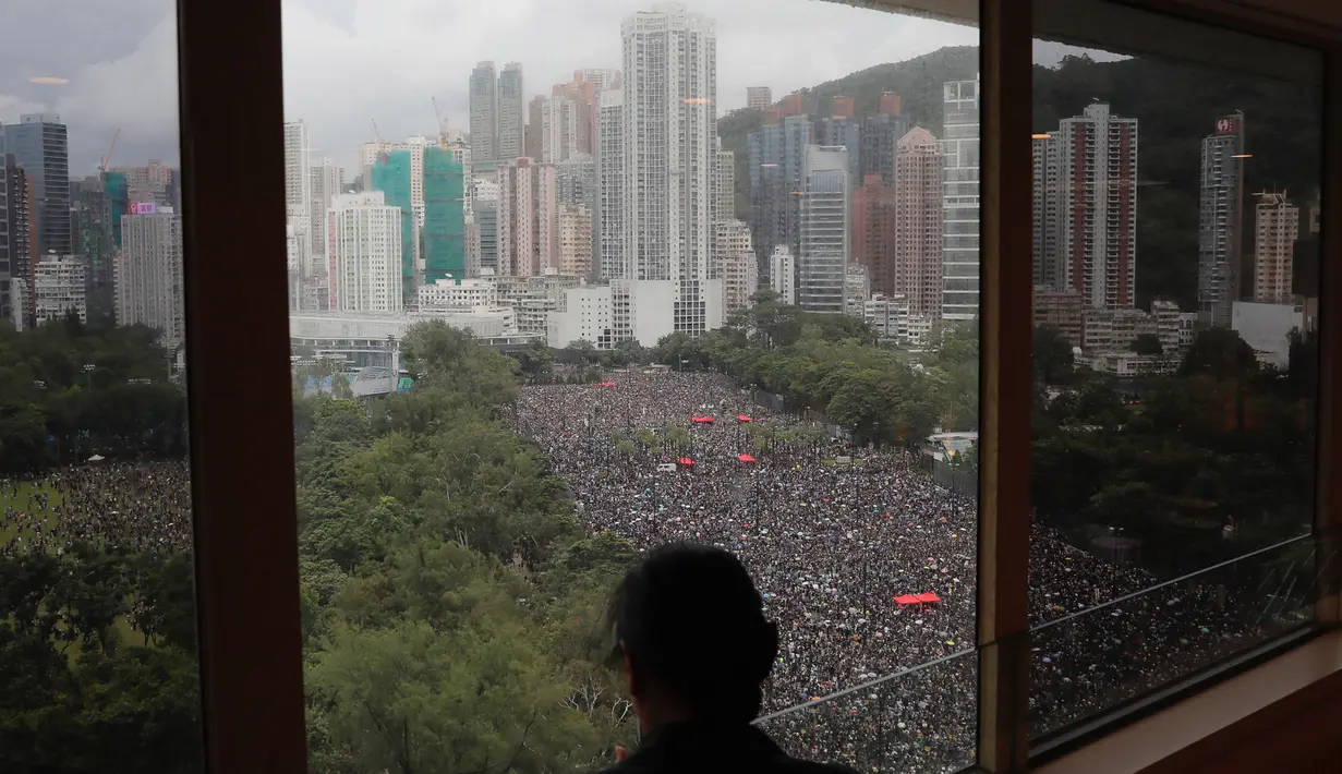 Seseorang berdiri dekat jendela melihat unjuk rasa di Victoria Park, Hong Kong, Minggu (18/8/2019). Puluhan ribu massa pro-demokrasi membawa payung saat hujan mengguyur Victoria Park dan sekitarnya. (AP Photo/Kin Cheung)