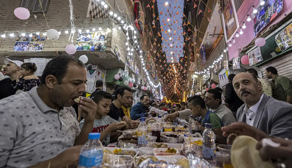 Umat muslim berkumpul di meja sepanjang jalan untuk berbuka puasa bersama dalam jamuan buka puasa massal pada hari ke-15 bulan suci Ramadhan di pinggiran Matariya, timur laut Kairo, Mesir, 16 April 2022. (Khaled DESOUKI/AFP)