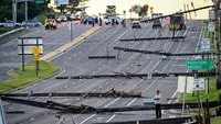 Pemandangan arah timur dari Route 97, seorang pria berdiri melihat tiang listrik yang tumbang di Route 140, Westminster, Maryland, Amerika Serikat, Selasa (8/8/2023). Tiang listrik bertumbangan setelah badai dahsyat melanda area tersebut pada Senin malam. (Jerry Jackson/The Baltimore Sun via AP)