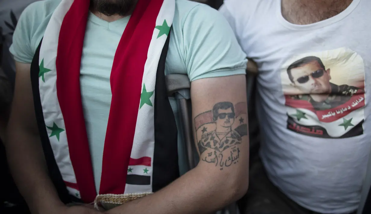 Seorang tentara Suriah yang terluka dengan tato Presiden Bashar Assad saat mereka merayakan kemenangannya di Omayyad Square, di Damaskus, Kamis (27/5/2021). Bashar al-Assad terpilih kembali untuk masa jabatan keempat sebagai presiden Suriah yang dilanda perang. (AP Photo/Hassan Ammar)
