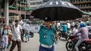 Seorang petugas polisi Bangladesh memegang payung untuk melindungi dirinya dari sengatan matahari saat mengatur lalu lintas di persimpangan jalan di Dhaka pada tanggal 12 Agustus 2024. (LUIS TATO/AFP)