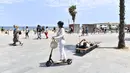 Seorang wanita mengendarai skuter listrik di kawasan pejalan kaki di Pantai Bogatell di Barcelona, Minggu (6/6/2021). Spanyol mengizinkan semua turis yang sudah divaksinasi corona memasuki negaranya mulai 7 Juni mendatang. (Pau BARRENA/AFP)