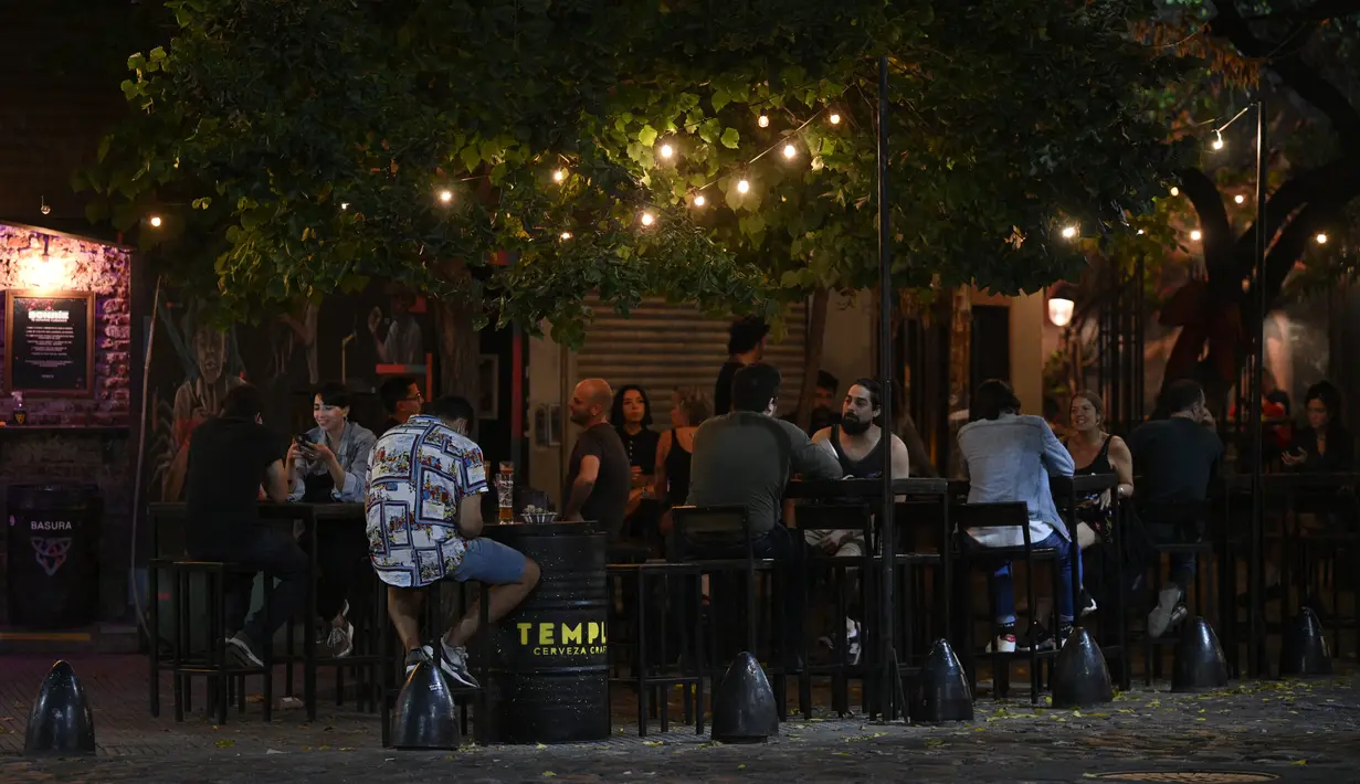 Orang-orang menikmati minuman sambil duduk di meja di trotoar di Buenos Aires, Argentina, Selasa (6/4/2021). Argentina mencatatkan rekor 20.780 kasus positif Covid-19 dalam sehari atau rekor tertinggi yang pernah dilaporkan sejak kasus pertama Covid-19 pada Maret 2020 lalu. (JUAN MABROMATA/AFP)