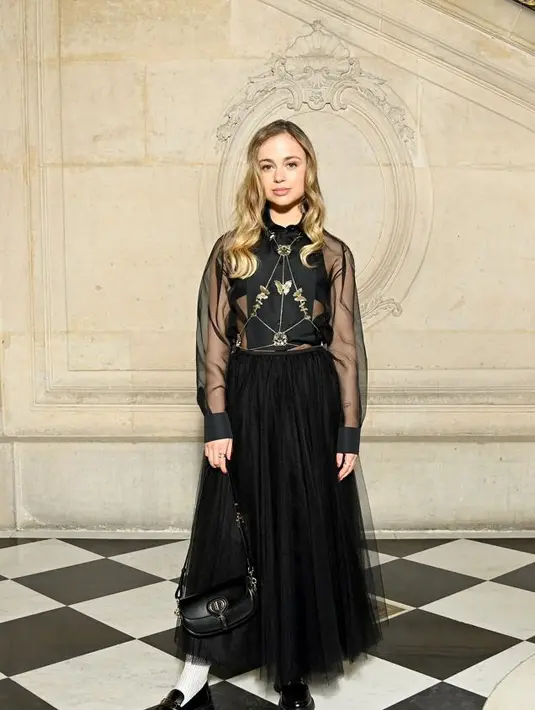 Model Amelia Windsor mengenakan kemeja sutra hitam Dior Cruise 2022 dengan rok tulle hitam dan perhiasan tubuh emas. Dia juga mengenakan tas Dior Bobby dan sepatu kulit hitam. (Dior)