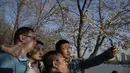 Pengunjung berswafoto dengan latar belakang bunga sakura yang bermekaran di Taman Yuyuantan, Beijing, 24 Maret 2019. Di taman tersebut ditanam sebanyak 2.000 pohon sakura dari 18 jenis yang bermekaran setiap musim semi pada akhir bulan Maret sampai April. (Nicolas ASFOURI / AFP)