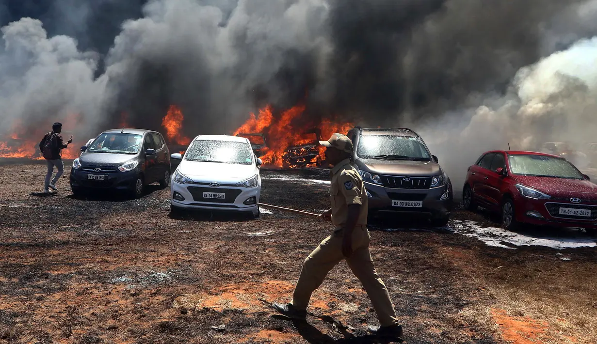 Petugas pemadam kebakaran berdiri dekat deretan mobil yang terbakar di area parkir pameran dirgantara Aero India 2019, Bangalore, India, Sabtu (23/2). Pejabat pemadam kebakaran menduga rumput kering memicu terjadinya kebakaran. (AP Photo/Parthi Bhan)