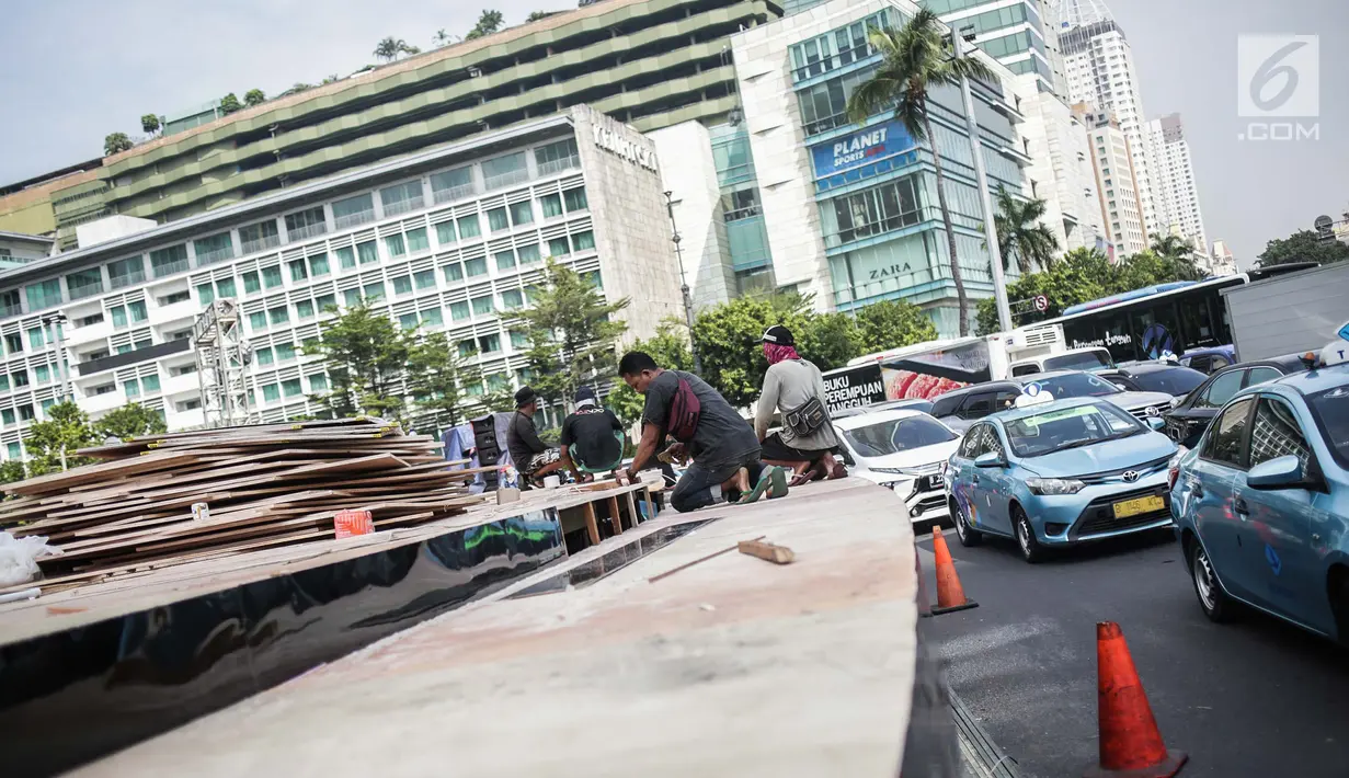 Kendaraan melintas di samping pekerja yang tengah menyelesaikan pembuatan panggung HUT ke-492 DKI di area Bundaran HI, Jakarta, Kamis (20/6/2019). Pemprov DKI Jakarta akan menggelar pesta rakyat di area Bundaran HI pada 22 Juni 2019. (Liputan6.com/Faizal Fanani)