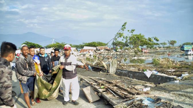 Warga mengevakuasi kantong jenazah berisi jasad korban tsunami di Palu, Sulawesi Tengah , Sabtu (29/9). Gelombang tsunami setinggi 1,5 meter yang menerjang Palu terjadi setelah gempa bumi mengguncang Palu dan Donggala. (AP Photo/Rifki)