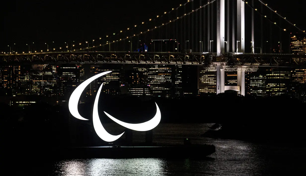 Simbol Paralimpiade menyala pada malam hari dengan latar belakang Jembatan Pelangi di tepi Pantai Odaiba, Tokyo, Jepang, 23 Agustus 2021. Paralimpiade Tokyo 2020 mulai 24 Agustus 2021 sampai 5 September 2021. (Charly TRIBALLEAU/AFP)