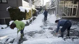 Warga menyingkirkan salju di luar rumah mereka di bangsal Meguro di Tokyo (23/1). Hujan salju membuat keberangkatan penerbangan dan melumpuhkan beberapa layanan kereta api di kota tersebut. (AFP Photo/Behrouz Mehri)