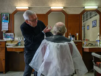 Penata rambut Roger Amilhastre (kiri), 90 tahun, memotong rambut Yves Desdoit di salon rambutnya, "Achillle coiffure masculin", di kota Saint-Girons, barat daya Prancis pada 16 April 2024. (Photo by Ed JONES / AFP)