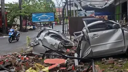 Pengendara motor melewati rongsokan mobil yang rusak akibat gempa bumi di Mamuju, Sulawesi Barat, Sabtu (16/1/2021). Petugas Badan Penanggulangan Bencana Daerah (BPBD) masih mendata jumlah kerusakan dan korban akibat gempa bumi tersebut. (AP Photo/Yusuf Wahil)