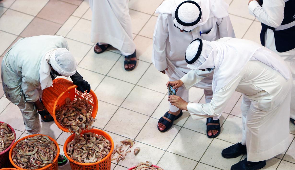 Seorang pria mengambil gambar udang selama pelelangan di pasar ikan di Kuwait City (8/8/2021). Pelelangan dibuka kembali di negara itu setelah enam bulan ditutup di tengah pandemi virus corona. (AFP/ Yasser Al-Zayyat)