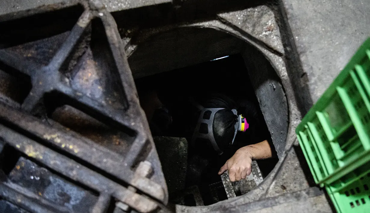 Demonstran turun ke pintu masuk selokan ketika mencoba mencari jalan untuk melarikan diri dari Universitas Politeknik Hong Kong di Hung Hom, 19 November 2019. Dengan lengan dilapisi plastik dan dilengkapi penerang seadanya, mereka mencoba mencari jalan keluar lewat selokan. (Anthony WALLACE/AFP)