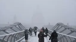Pejalan kaki melintasi jembatan milenium dengan latar katedral St Paul saat hujan salju turun di London (27/2). (AFP Photo/Daniel Leal-Olivas)