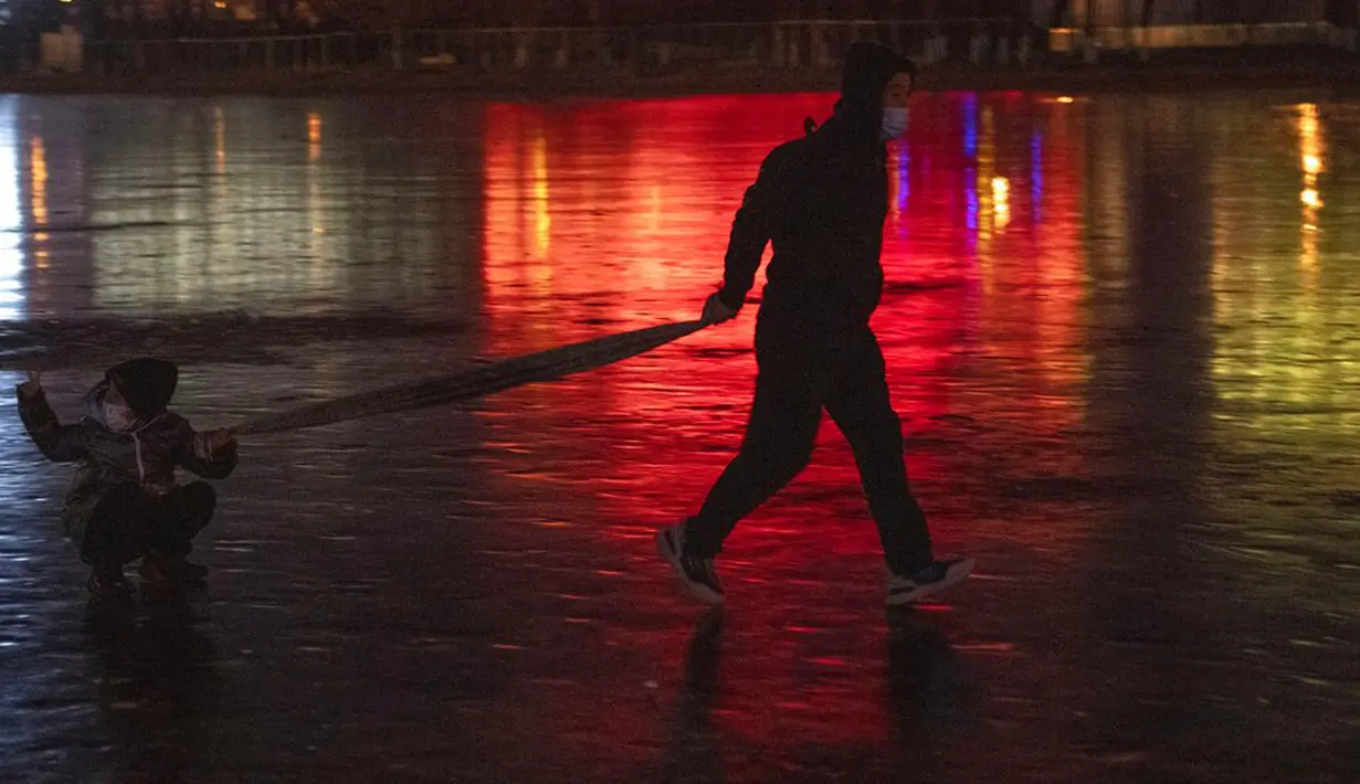 Warga yang mengenakan masker menarik seorang anak melintasi danau beku dekat Olympics Green di Beijing, China, 3 Januari 2022. Libur Tahun Baru dimanfaatkan warga untuk bermain ice skating di sungai dan danau yang membeku. (AP Photo/Ng Han Guan)