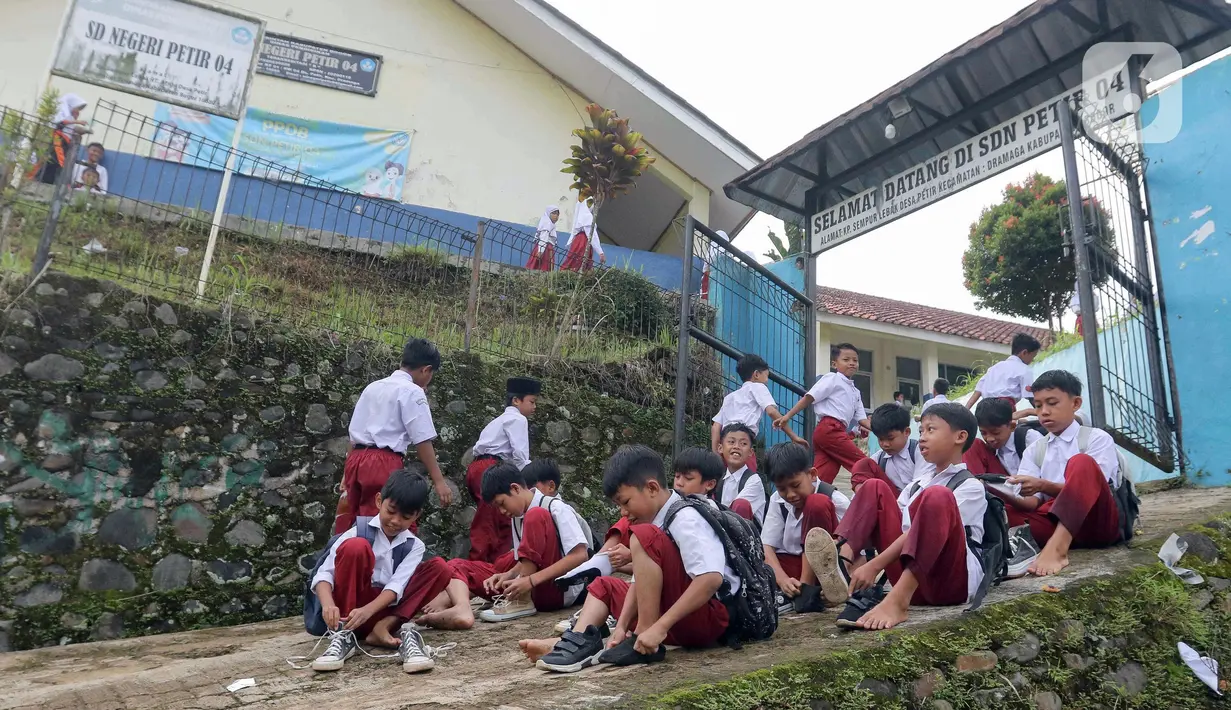 Beberapa pelajar Sekolah Dasar (SD) Negeri 04 Kampung Sempur Lebak, Desa Petir, Kecamatan Dramaga, Kabupaten Bogor, Jawa Barat memam\kai sepatu mereka sebelum masuk halaman sekolah setelah sebelumnya menyeberangi Sungai Cihideung. (Liputan6.com/Herman Zakharia)